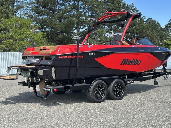 Slide: The Image of 2025 Malibu 23 LSV boat in red and black on a trailer, parked outdoors. - 23