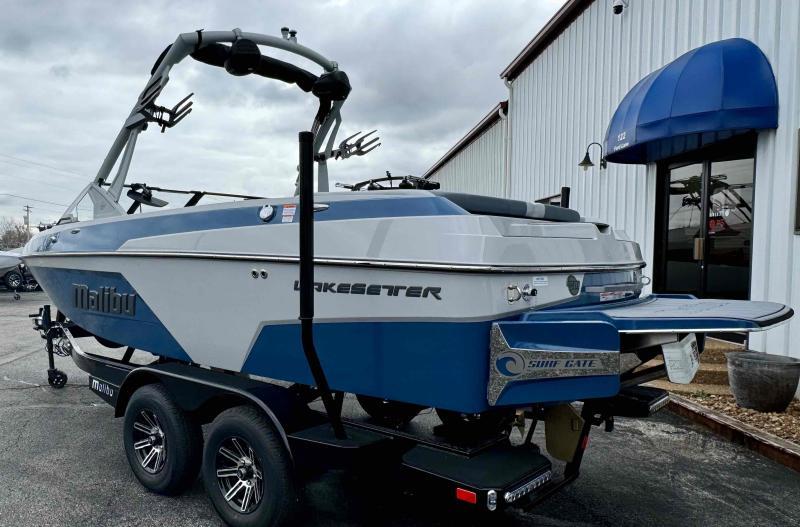 Slide: The Image of 2024 Malibu 20 VTX Wakesetter boat on a trailer outside a building. - 13