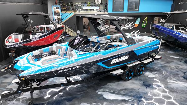 Slide: The Image of 2021 Malibu Wakesetter 24 MXZ boat in showroom, vibrant blue and black design. - 2