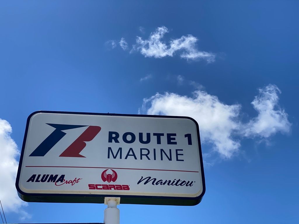 Slide: The Image of Route 1 Marine dealership sign with Alumacraft, Scarab, and Manitou logos under blue sky. - 27