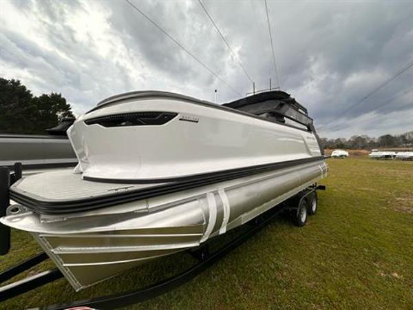 Slide: The Image of 2024 Manitou 24 Explore pontoon boat on a trailer under cloudy skies. - 0