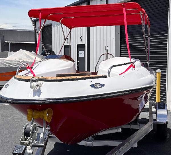 Slide: The Image of 2025 MarinBoat Tango with red canopy on trailer, parked outside a warehouse. - 2