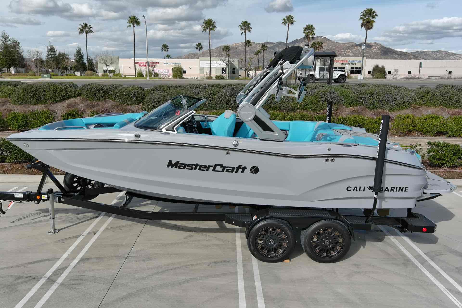 Slide: The Image of 2023 MasterCraft X22 boat on trailer, side view, with blue interior, parked outdoors. - 1