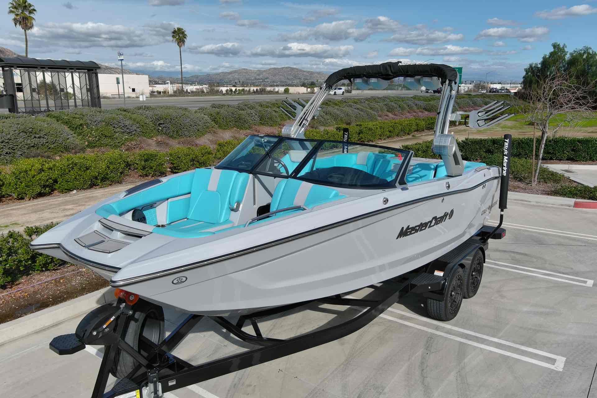 Slide: The Image of 2023 MasterCraft X22 boat with turquoise interior on a trailer in a parking lot. - 2