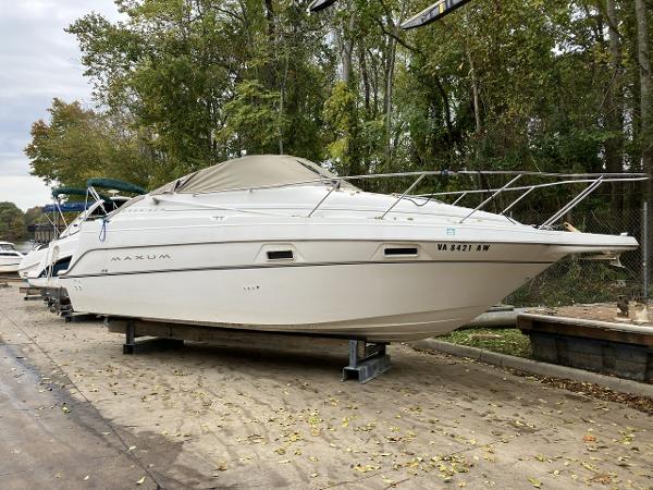 Slide: The Image of 2000 Maxum 2400 SCR boat on dry dock, white exterior, covered, surrounded by trees. - 1