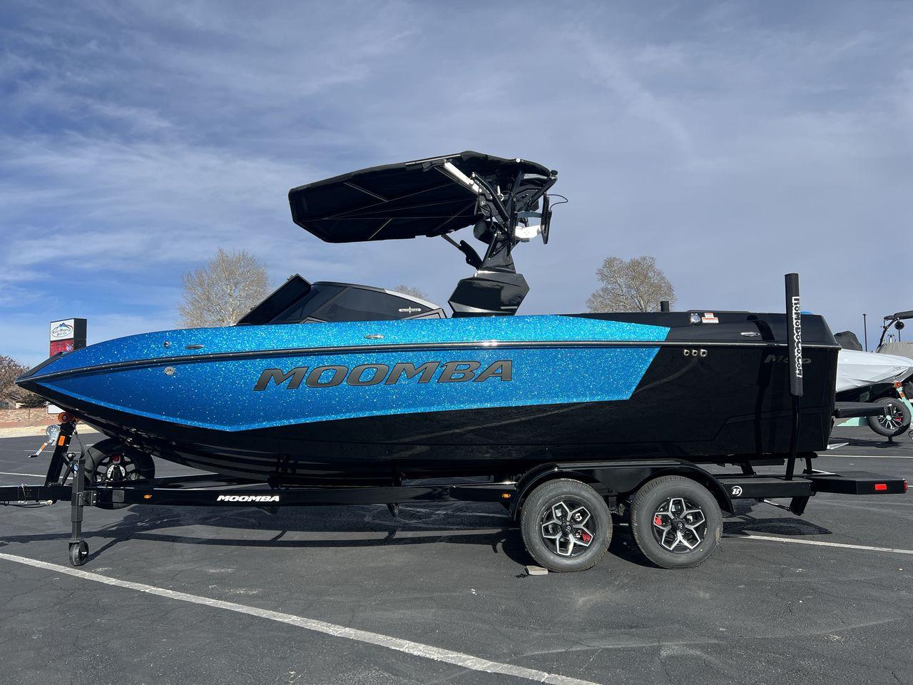 Slide: The Image of 2025 Moomba Mojo boat in vibrant blue, parked on a trailer under a clear sky. - 2