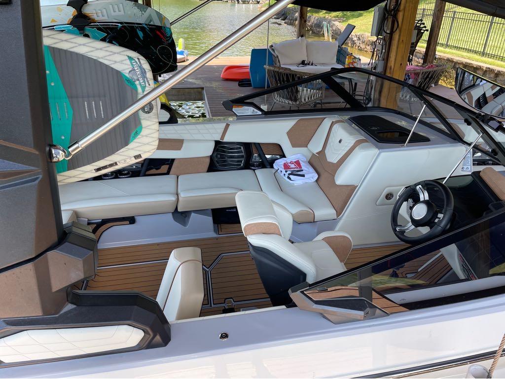 Slide: The Image of 2023 Nautique G23 boat interior with seating and steering wheel, docked by the lake. - 23
