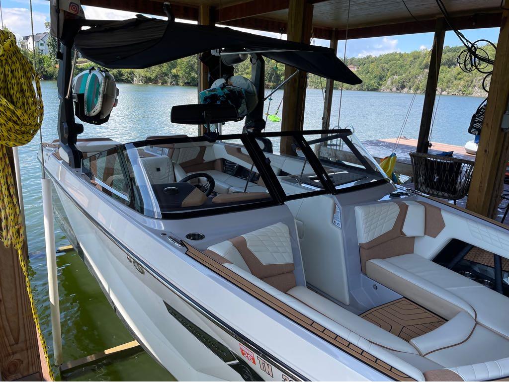 Slide: The Image of 2023 Nautique G23 boat docked in a covered marina with scenic lake view. - 31