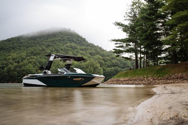 Slide: The Image of 2023 Nautique Super Air Nautique G23 Paragon boat on a serene lake with lush green hills. - 1