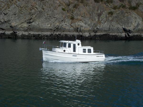 Slide: The Image of 2025 Nordic Tug 26 cruising near rocky shoreline. - 0