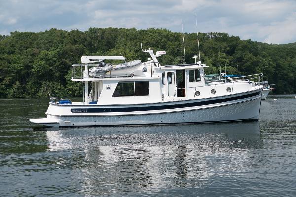 Slide: The Image of 2025 Nordic Tug 40 boat on a calm lake with a forested background. - 12