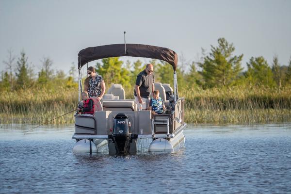 Slide: The Image of 2023 Premier 220 Castaway pontoon boat on a serene lake with people fishing. - 4