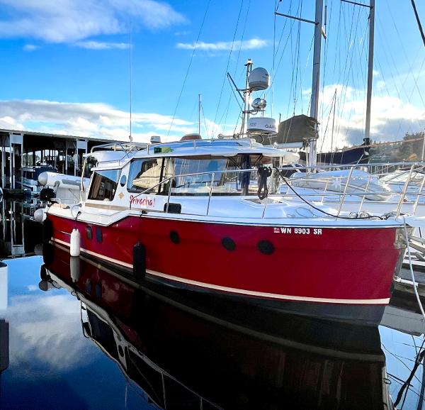 The Image of 2019 Ranger Tugs R-29S boat in marina, red hull, clear sky reflection. - 0