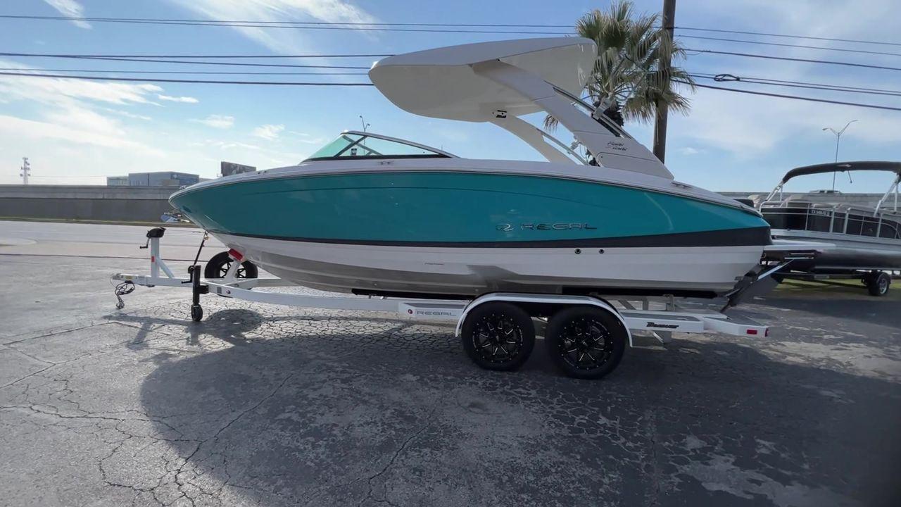 Slide: The Image of 2023 Regal LS6 Surf boat on a trailer, teal and white exterior. - 5