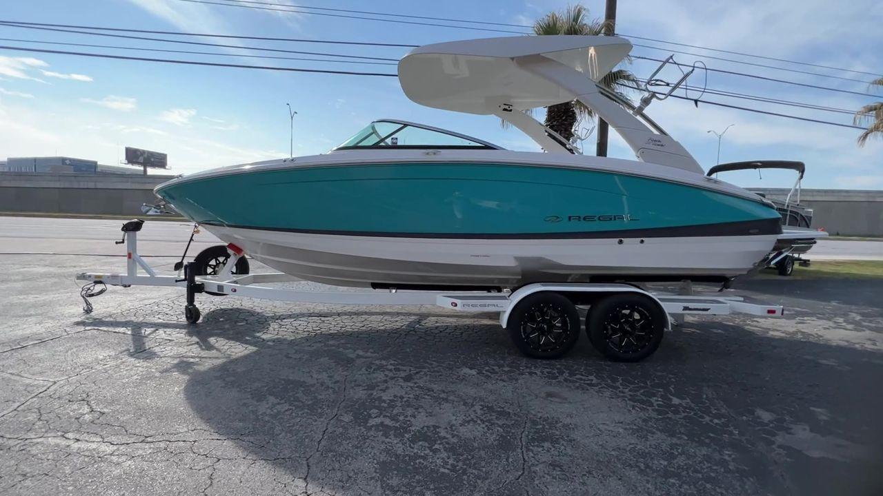 Slide: The Image of 2023 Regal LS6 Surf boat on trailer, side view, teal and white color. - 7