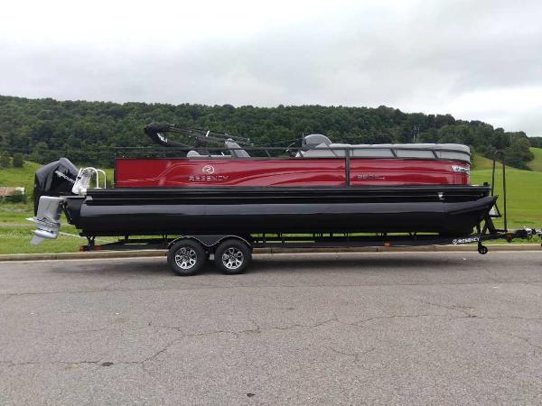 Slide: The Image of 2024 Regency 250 DL3 pontoon boat on trailer, parked on road with scenic background. - 0