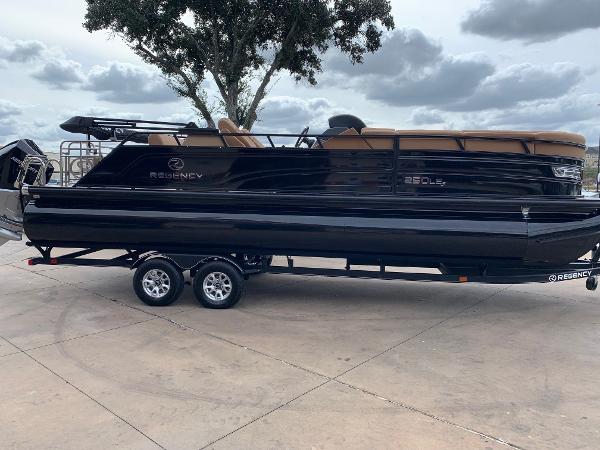 Slide: The Image of 2024 Regency 250 LE3 Sport pontoon boat on trailer, parked outdoors. - 0