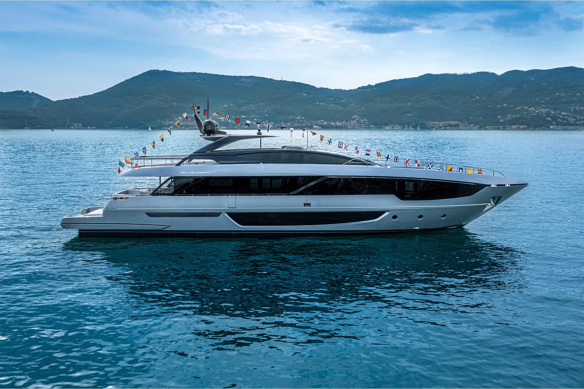 Slide: The Image of 2024 Riva 102' Corsaro Super luxury yacht on calm waters with scenic mountain backdrop. - 0