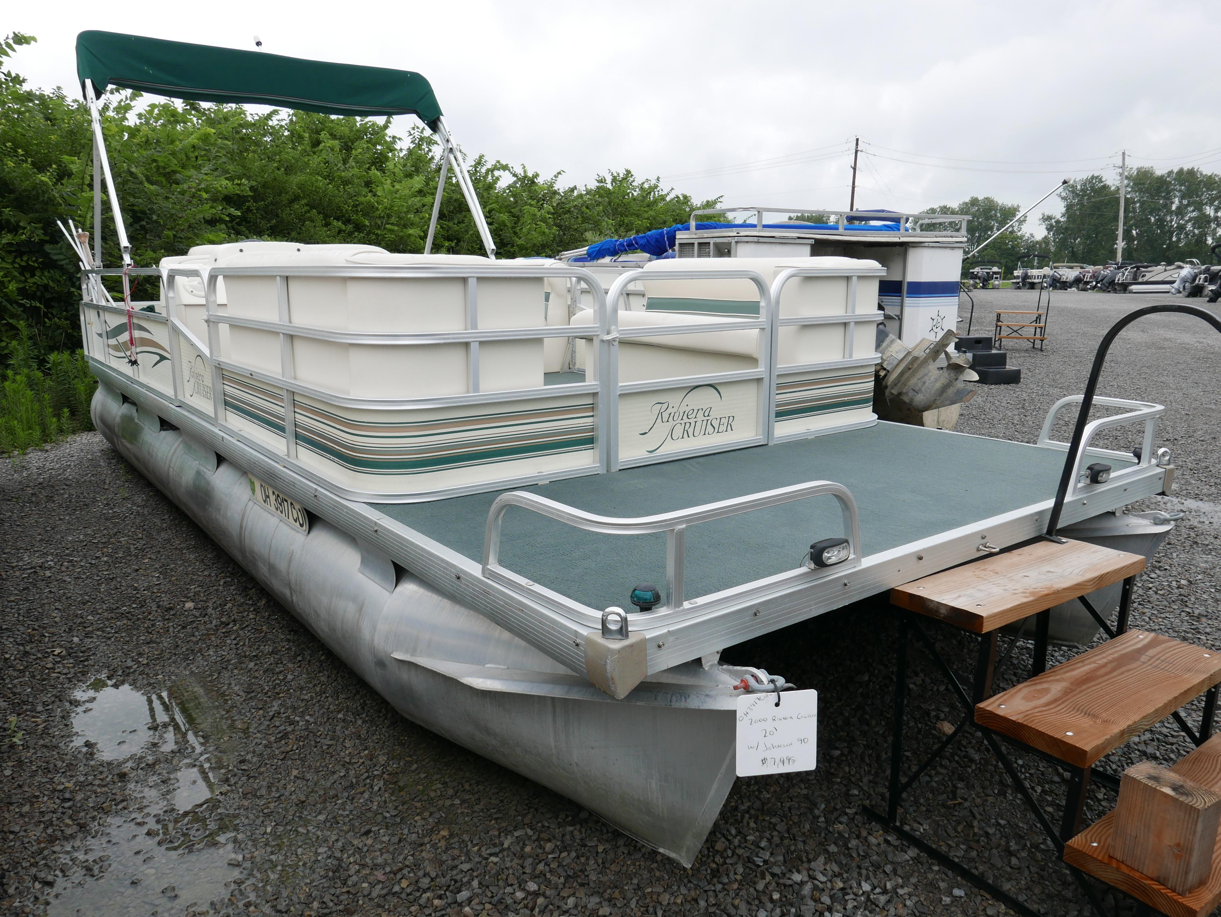 Slide: The Image of 2000 Riviera Cruiser pontoon boat with green canopy, parked on gravel. - 1