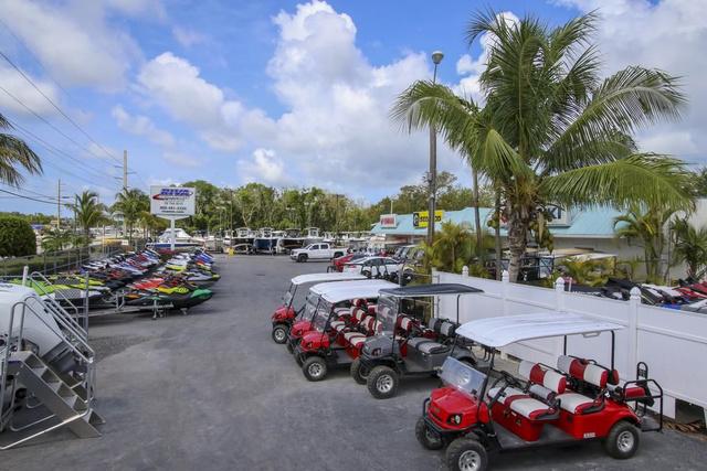 Slide: The Image of Outdoor dealership with 2024 Robalo 206 Cayman boats and red golf carts under palm trees. - 49
