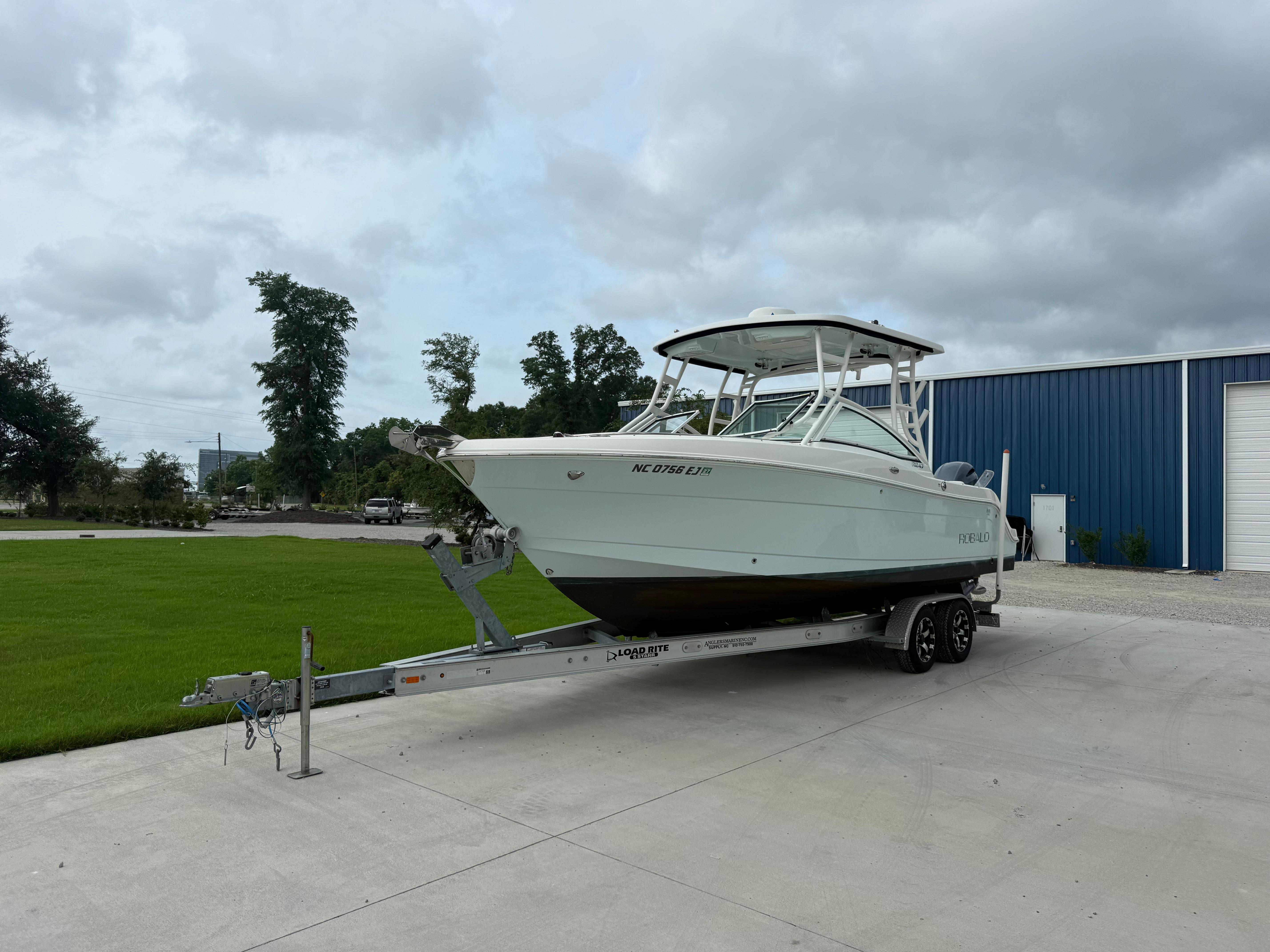 Slide: The Image of 2018 Robalo R247 Dual Console boat on trailer, parked near blue building. - 1