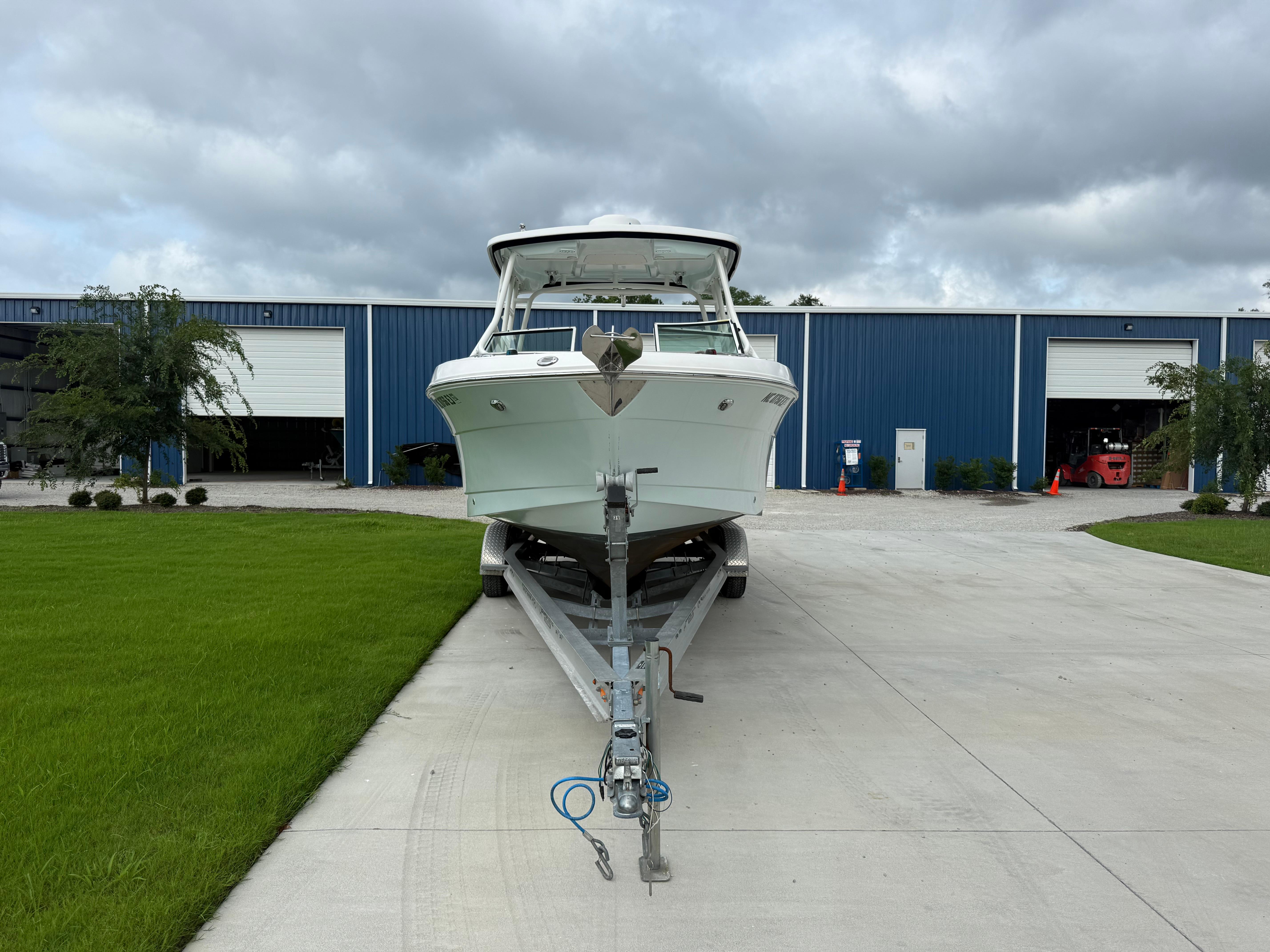 Slide: The Image of 2018 Robalo R247 Dual Console boat on trailer, parked outside blue warehouse. - 2