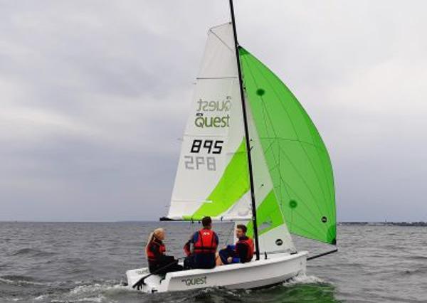 Slide: The Image of 2023 RS Quest sailboat with green sail on open water. - 0