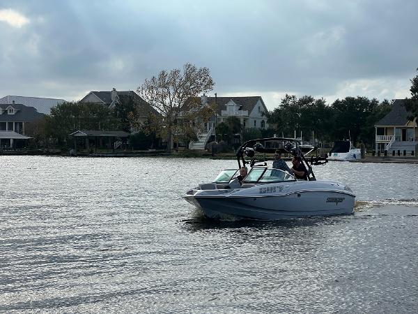 Slide: The Image of 2023 Sanger 231 SL boat cruising on a lake near waterfront homes. - 25
