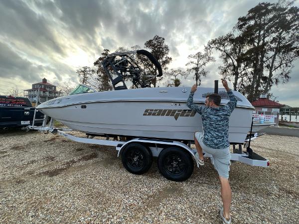 Slide: The Image of Man climbing onto a 2023 Sanger 231 SL boat on a trailer. - 4
