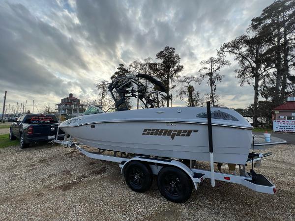 Slide: The Image of 2023 Sanger 231 SL boat on a trailer, parked near a lake with a cloudy sky. - 5