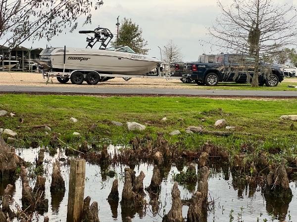Slide: The Image of 2023 Sanger 231 SL boat on trailer near a pond, parked beside a black truck. - 7