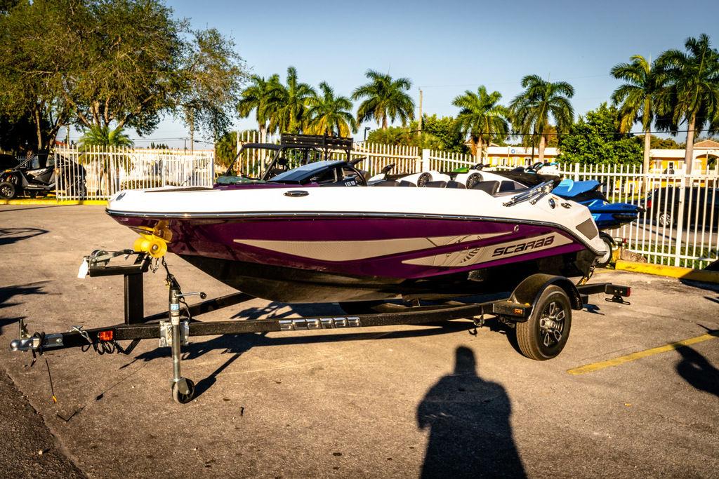 Slide: The Image of 2023 Scarab 165 ID boat on a trailer in a sunny parking lot. - 1