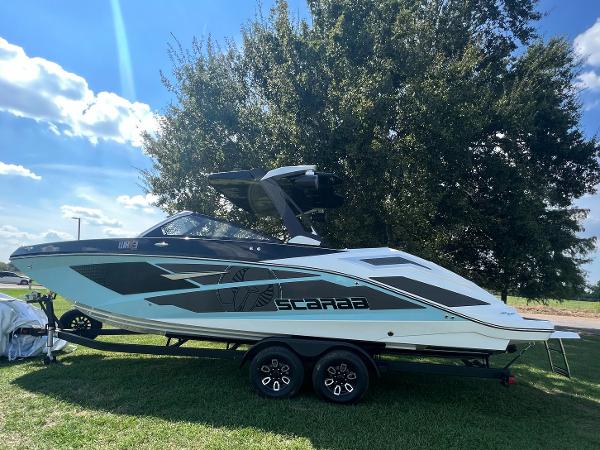 Slide: The Image of 2024 Scarab 285 ID boat on a trailer, parked on grass with trees in the background. - 7