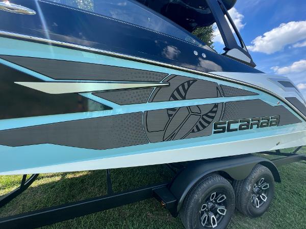 Slide: The Image of 2024 Scarab 285 ID boat side view with stylish graphics and dual-axle trailer. - 8