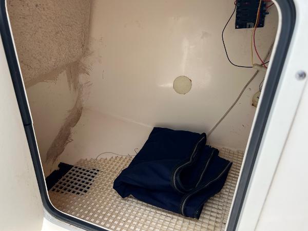 Slide: The Image of Interior of a 2000 Sea Hunt Escape 200 boat storage compartment with wiring and folded cover. - 14