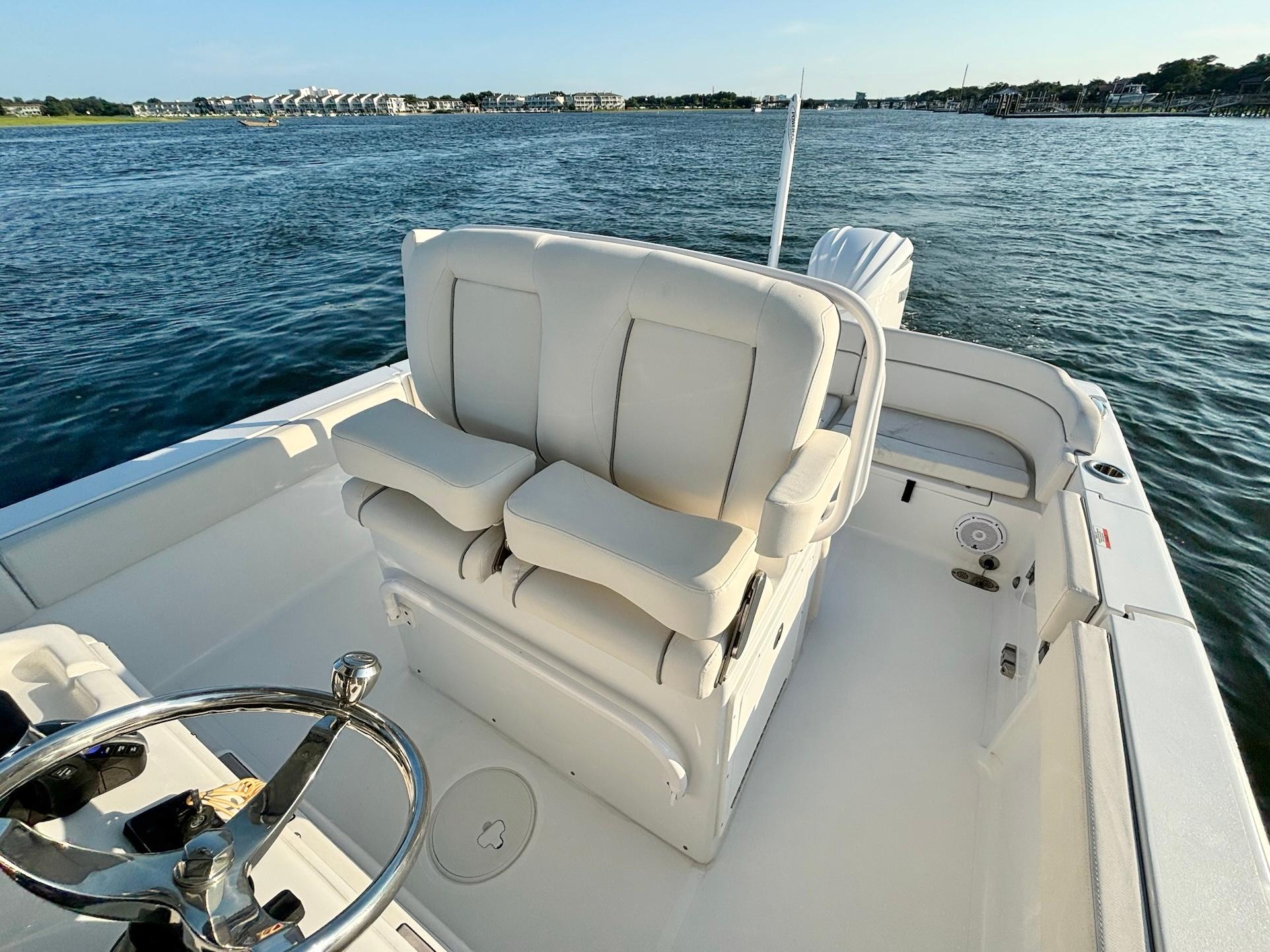 Slide: The Image of 2023 Sea Hunt Escape 25 boat interior with white seating and steering wheel on calm water. - 10