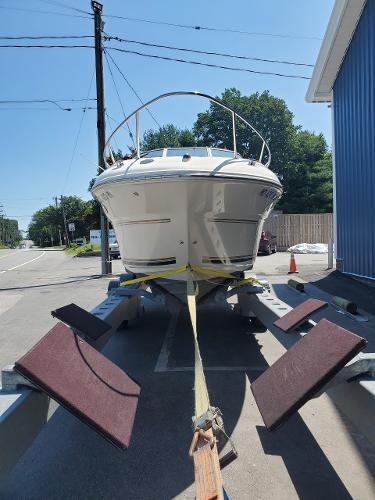 Slide: The Image of 2001 Sea Ray 245 Weekender boat on trailer, parked outdoors near a blue building. - 6