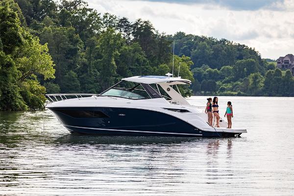 Slide: The Image of 2023 Sea Ray Sundancer 320 yacht on a serene lake with people on deck. - 0