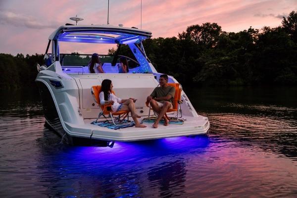 Slide: The Image of 2023 Sea Ray Sundancer 320 at sunset with blue underwater lights and people relaxing. - 8