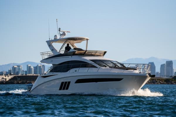 Slide: The Image of 2015 Sea Ray 510 Fly yacht cruising on open water with city skyline backdrop. - 24
