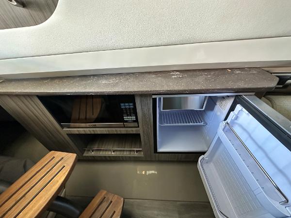Slide: The Image of Interior of 2023 Sea Ray SLX 400 OB with open mini fridge and wooden cabinetry. - 25