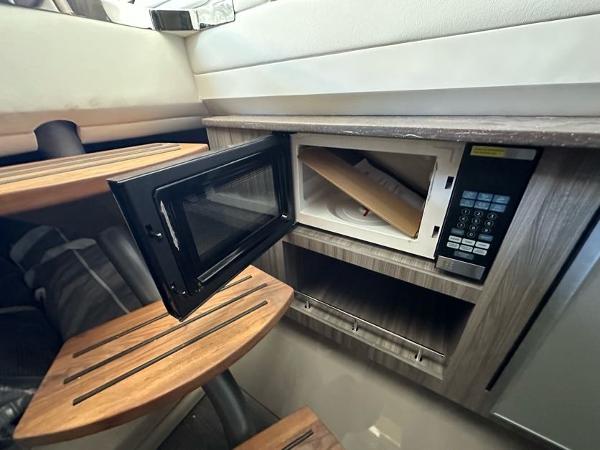 Slide: The Image of 2023 Sea Ray SLX 400 OB interior with open microwave and wooden steps. - 26