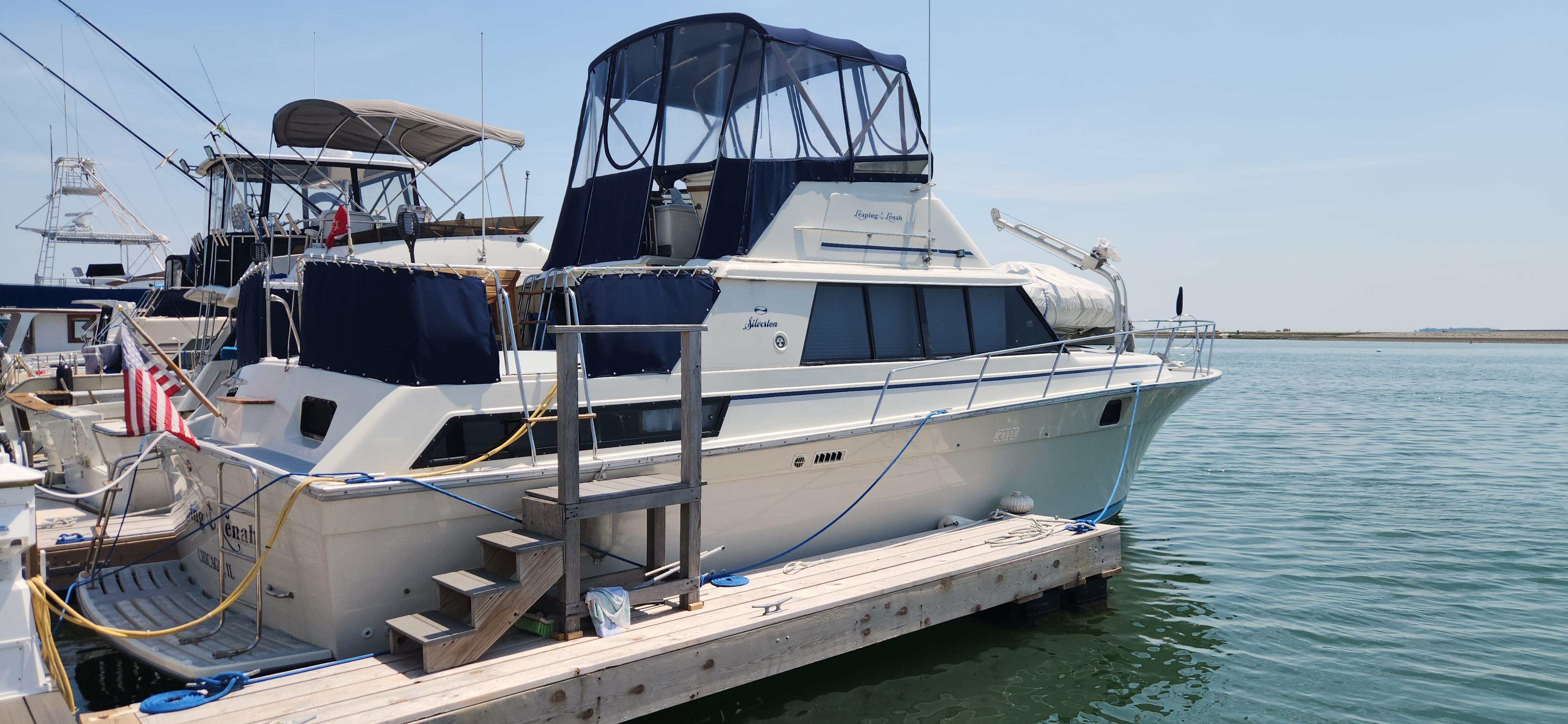 Slide: The Image of 1983 Silverton 40 Aft Cabin yacht docked at marina, featuring blue canopy and American flag. - 1