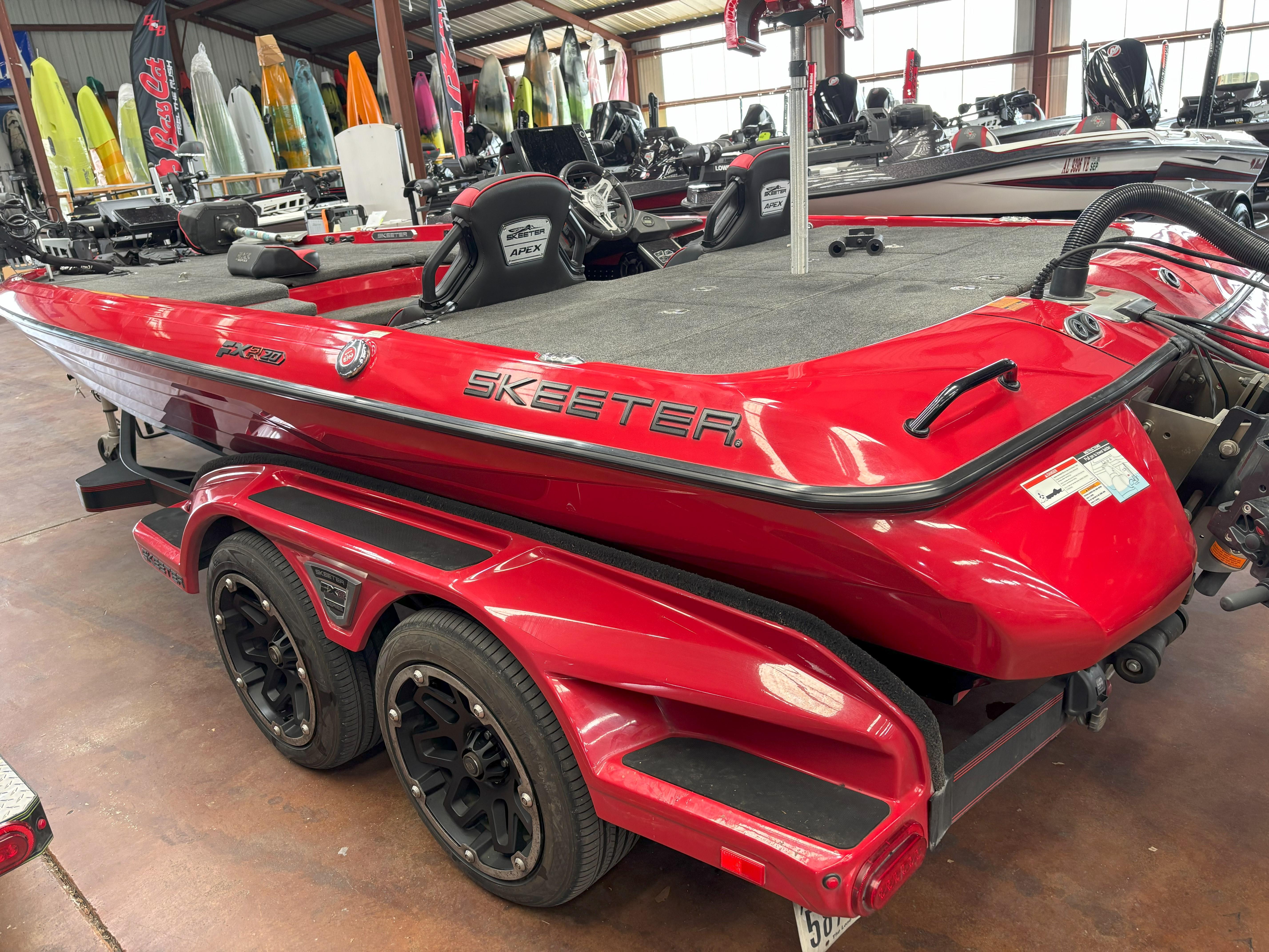 Slide: The Image of Red 2020 Skeeter FXR20 Apex boat in showroom, featuring sleek design and dual-axle trailer. - 1
