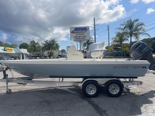 Slide: The Image of 2023 Skeeter SX210 boat on trailer at dealership, palm trees in background. - 2