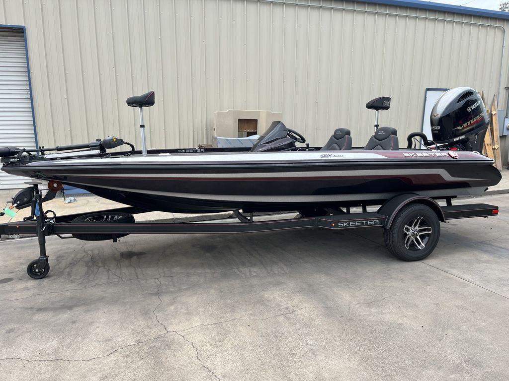 Slide: The Image of 2024 Skeeter ZX150 fishing boat on trailer, parked outside a warehouse. - 0
