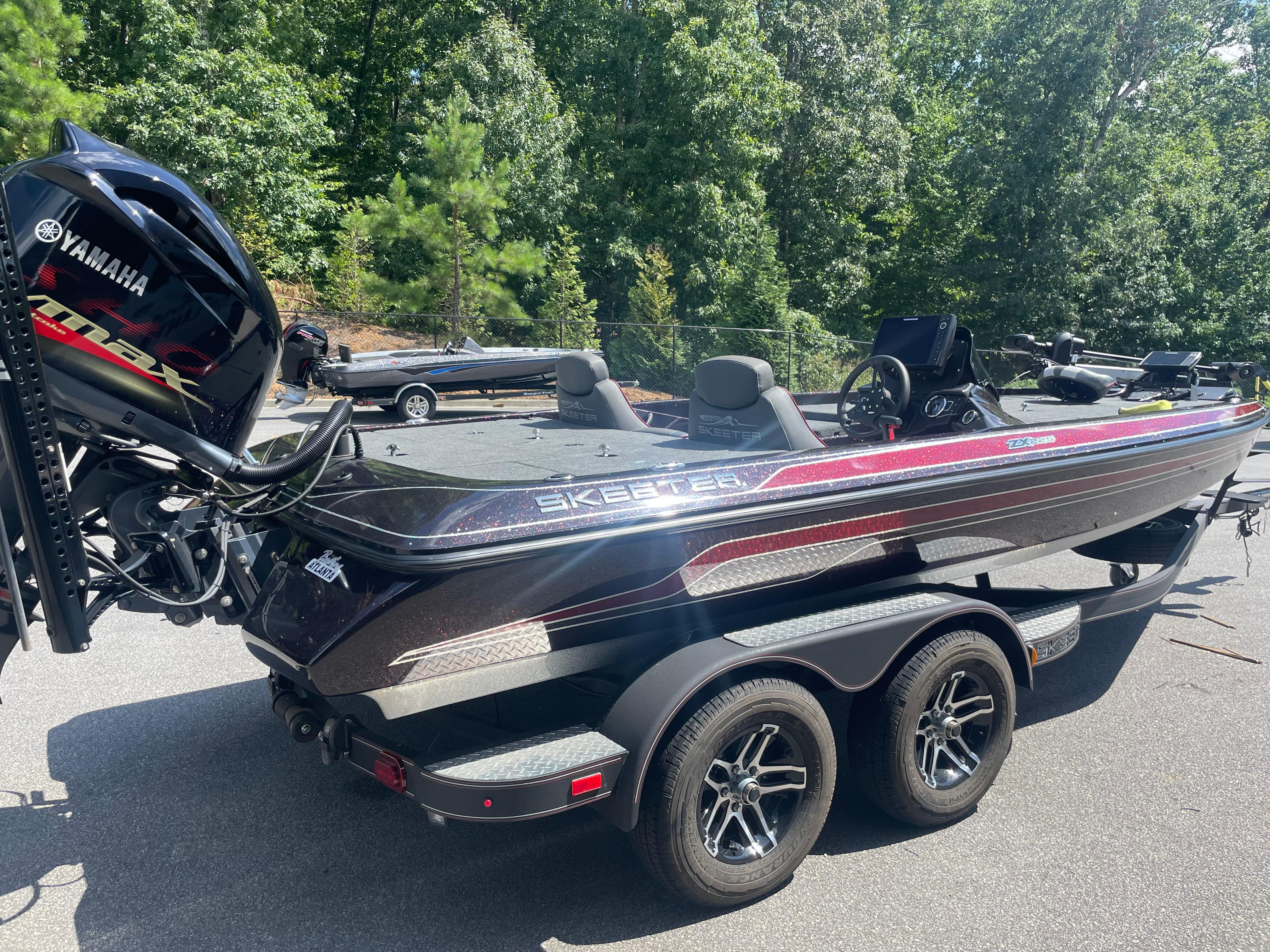 Slide: The Image of 2020 Skeeter ZX 225 bass boat with Yamaha engine, parked on a trailer in a wooded area. - 2