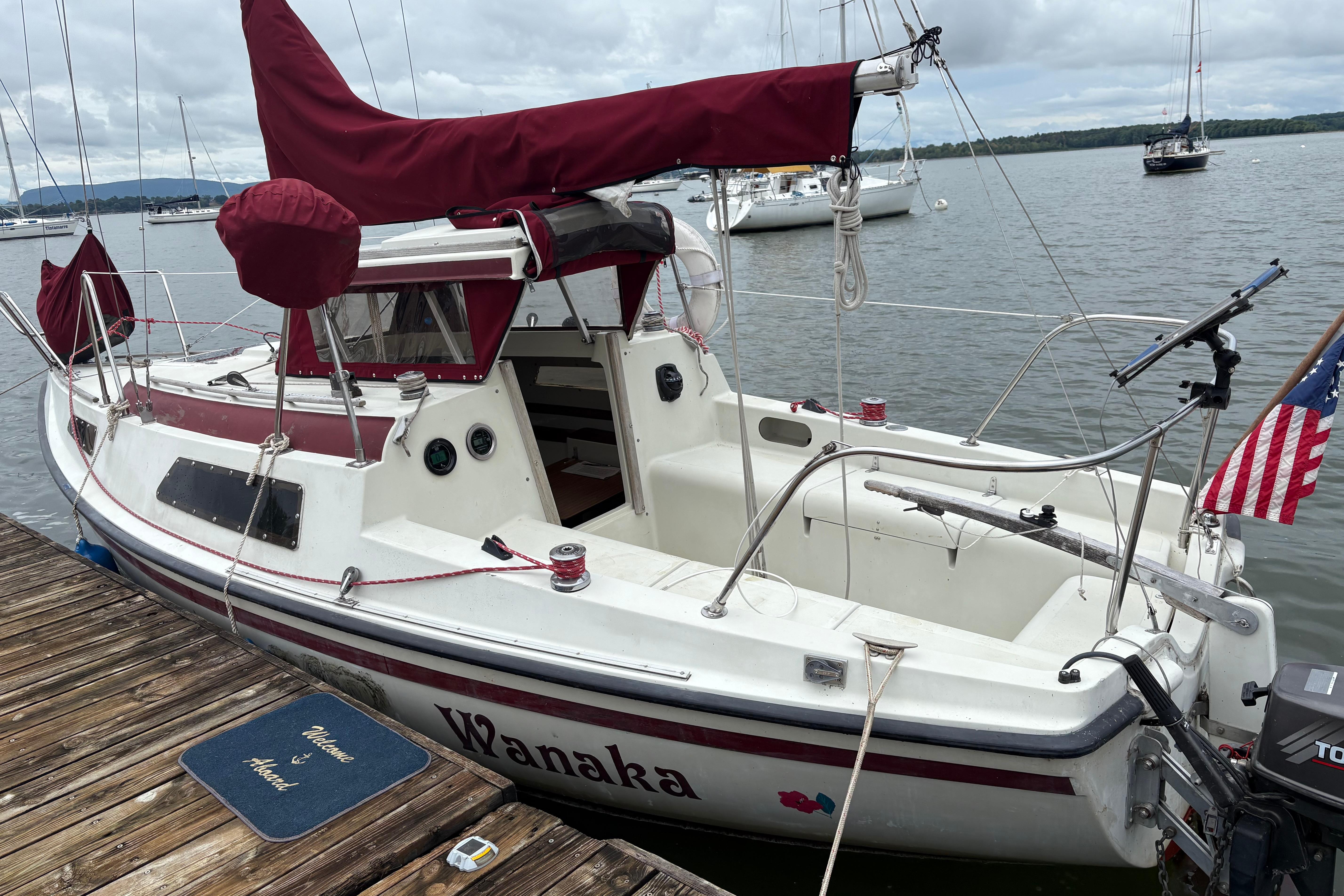 Slide: The Image of 1983 Sonic 23 sailboat docked, featuring maroon sails and American flag. - 0