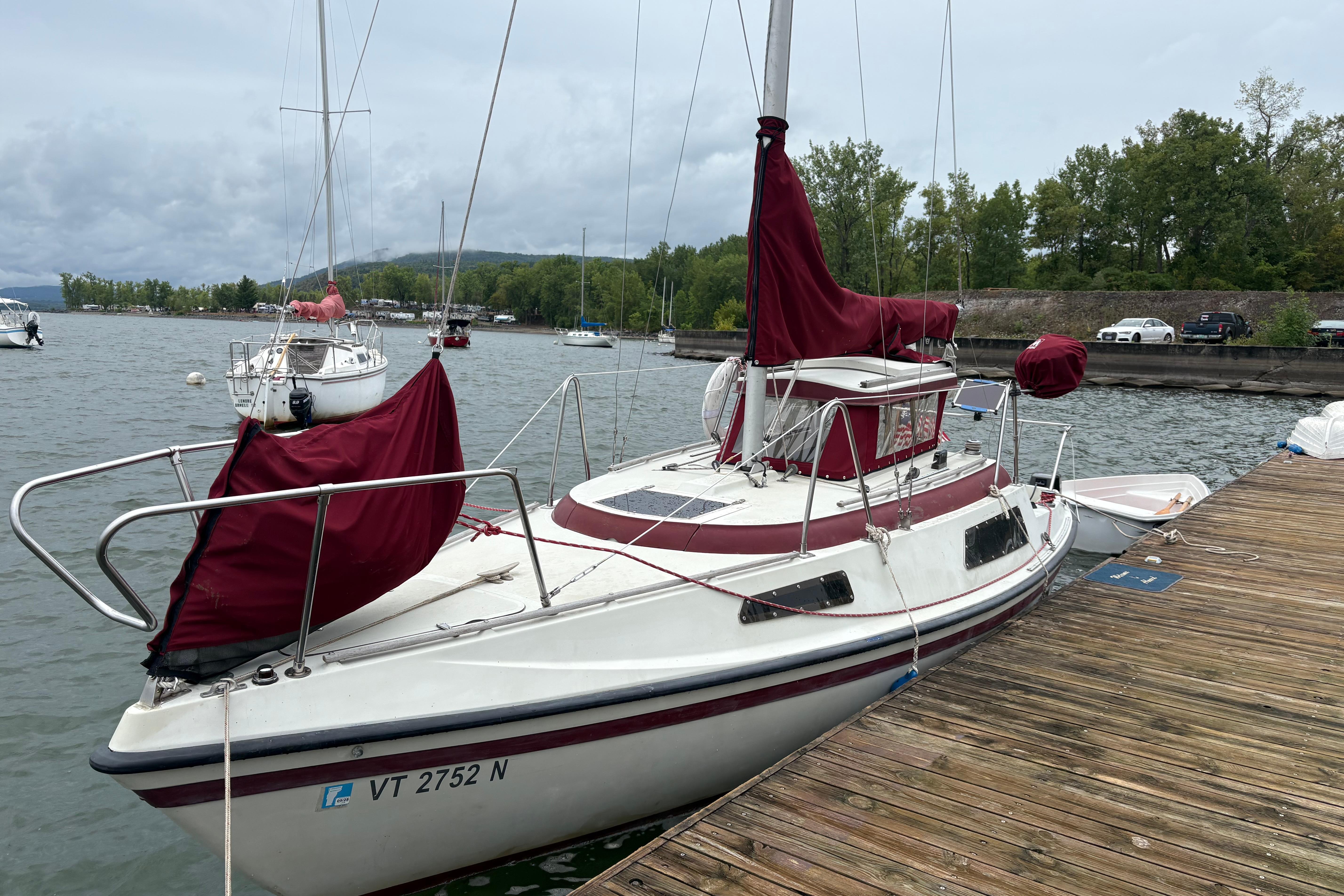 Slide: The Image of Sonic 23 sailboat from 1983 docked on a wooden pier, with maroon covers. - 1