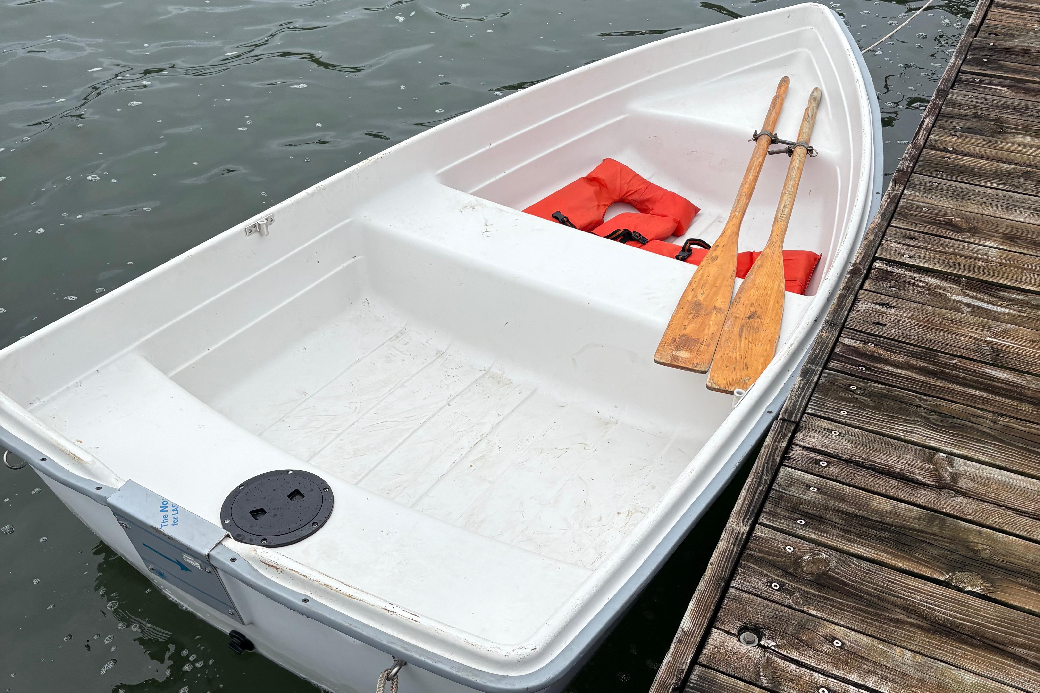 Slide: The Image of White Sonic 23 rowboat from 1983 with wooden oars and life jackets docked by wooden pier. - 13
